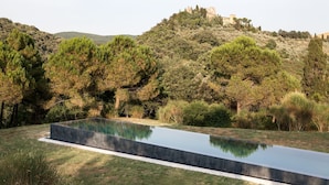 Ein rechteckiger Infinity-Pool mit freiem Blick auf die umliegende Landschaft, darunter Bäume und ein Hügel mit Ruinen.