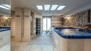 Uma área de spa com duas banheiras de hidromassagem, paredes de pedra e um chuveiro em gabinete de vidro.