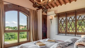 Um quarto com uma janela grande, uma cama com roupas de cama, um abajur e teto de madeira.