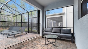 Eine moderne Terrassengruppe im Freien mit Glasveranda, einer grauen Couch und einem runden Tisch.