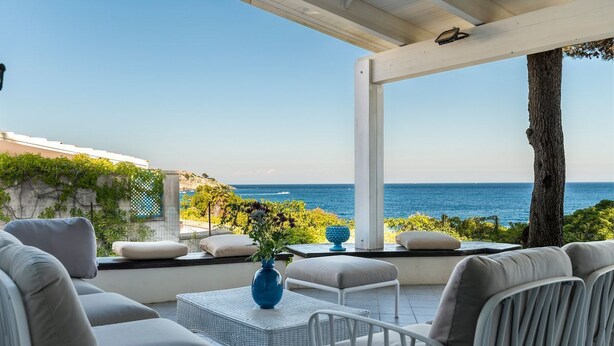 Une terrasse avec des meubles d’extérieur, un vase rempli de fleurs et une vue sur la mer.
