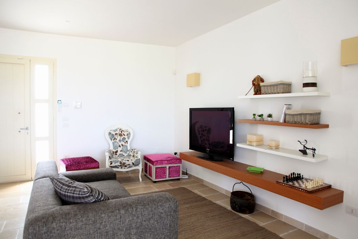 Una sala de estar con un sofá gris, una televisión, estanterías con objetos decorativos y una mesita con un juego de ajedrez.
