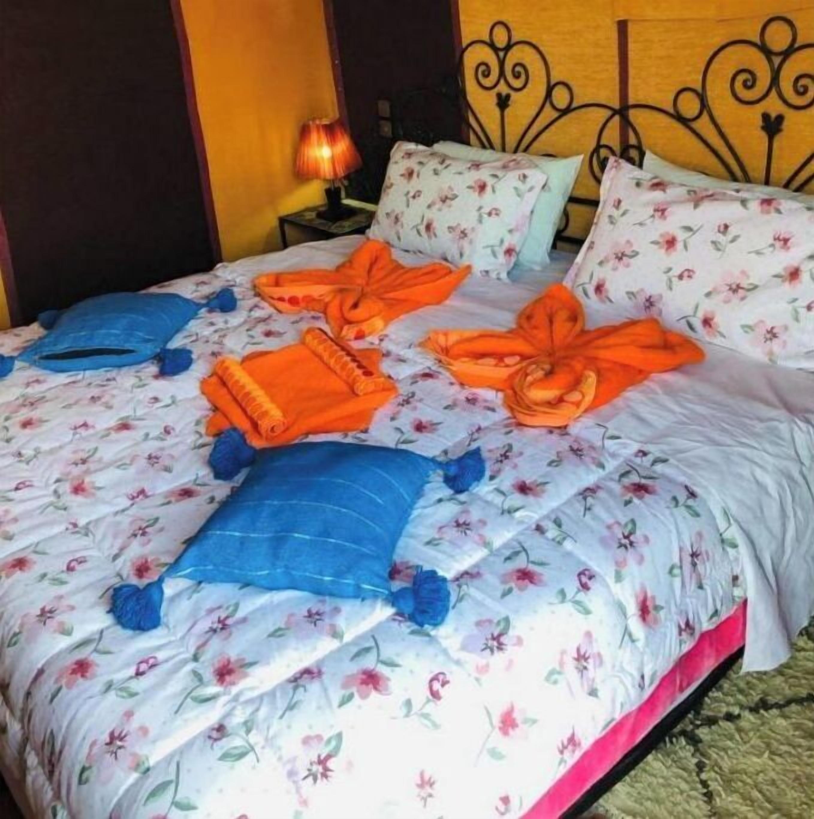 A bed with floral bedding, blue and orange pillows, and a metal headboard.