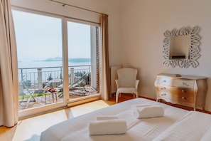 A hotel room with a bed, a chair, a dresser, and a balcony with a view of the water.