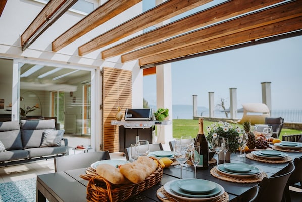 A dining area with a table set for a meal, a grill, and a view of the sea.