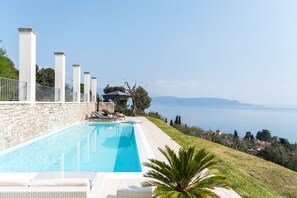 A swimming pool with lounge chairs and a stone wall, overlooking a body of water.