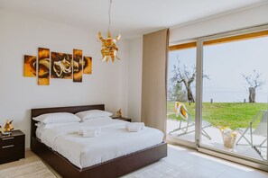 Une chambre dotée d’un grand lit, d’une table de chevet, d’une lampe fixée au mur et offrant une vue sur l’extérieur grâce à une porte-fenêtre coulissante.