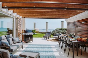 En udendørs terrasse med grill, siddepladser og et spisebord dækket til et måltid.