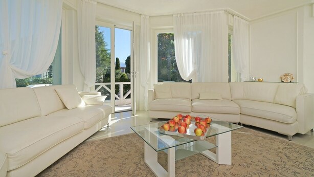 Amplia sala de estar con dos sofás blancos, una mesa de centro de cristal con manzanas y vistas a zonas verdes a través de grandes ventanales.