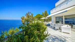 A modern outdoor patio with white wicker furniture, a pool, and a view of the sea.