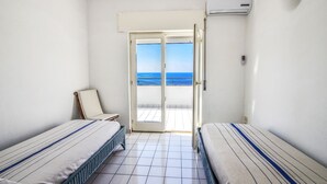 A hotel room with two beds, a balcony, and a view of the sea.