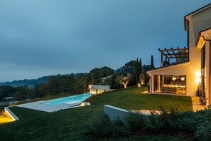 Ein modernes Haus mit Swimmingpool, einem gepflegten Rasen und einer Pergola.