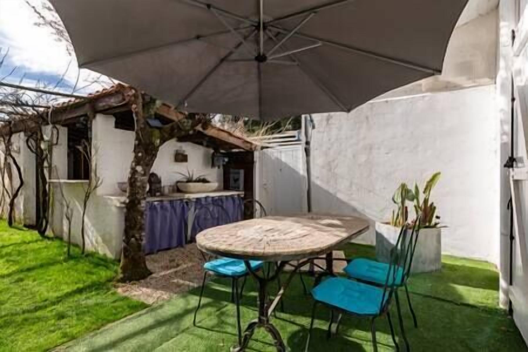Een terras met een ronde tafel en blauwe stoelen, omgeven door een witte muur en een boom.