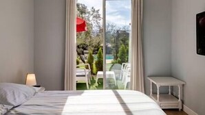 A bedroom with a bed, a nightstand, a small table, and a sliding glass door leading to an outdoor area with a pool and chairs. - House heated pool walking beach animals Ok (Labenne)