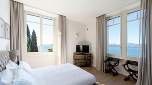 A hotel room with a large bed, a television, a small table, and a view of the sea.