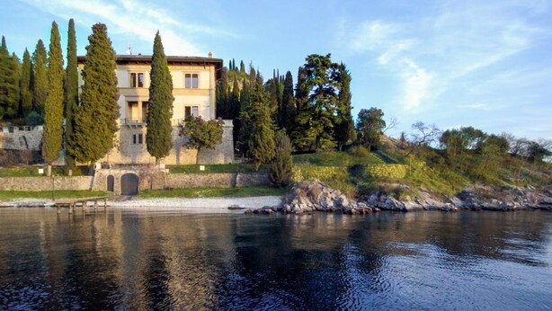 A large, multi-story building with a stone facade, situated beside a calm river.