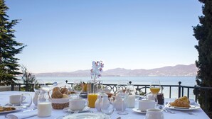 A breakfast table set with various food items and drinks, overlooking a scenic view of the sea and mountains.