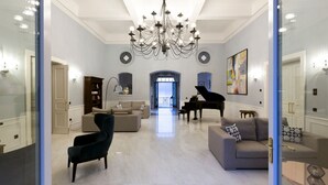 A spacious living room with a grand chandelier, a grand piano, and a modern fireplace.