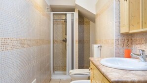 Een smalle badkamer met betegelde wanden, een douchecabine, een toilet en houten kasten.