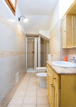 A narrow bathroom with tiled walls, a shower enclosure, a toilet, and wooden cabinets. - Torre del Drago - Three Bedroom Villa, Sleeps 6 (Marina di Felloniche)