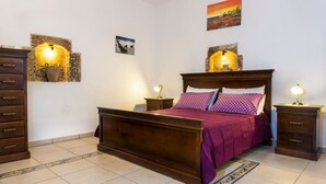 Een slaapkamer met een houten bed, twee nachtkastjes met lampen, een kaptafel en decoratieve wandkunst.