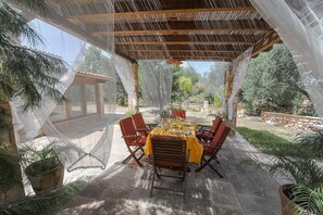 An outdoor patio with a table set for dining, surrounded by chairs, under a pergola with a netted roof. - Torre del Drago - Three Bedroom Villa, Sleeps 6 (Marina di Felloniche)