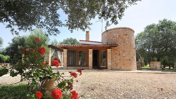 A rustic stone building with a circular tower, surrounded by a gravel area and red flowers in the foreground. - Torre del Drago - Three Bedroom Villa, Sleeps 6 (Marina di Felloniche)