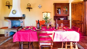 A dining room with a red tablecloth, wooden chairs, a fireplace, and a cabinet. - Torre del Drago - Three Bedroom Villa, Sleeps 6 (Marina di Felloniche)