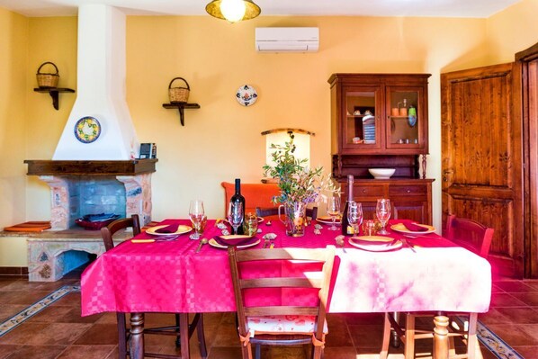 A dining room with a red tablecloth, wooden chairs, a fireplace, and a cabinet. - Torre del Drago - Three Bedroom Villa, Sleeps 6 (Marina di Felloniche)