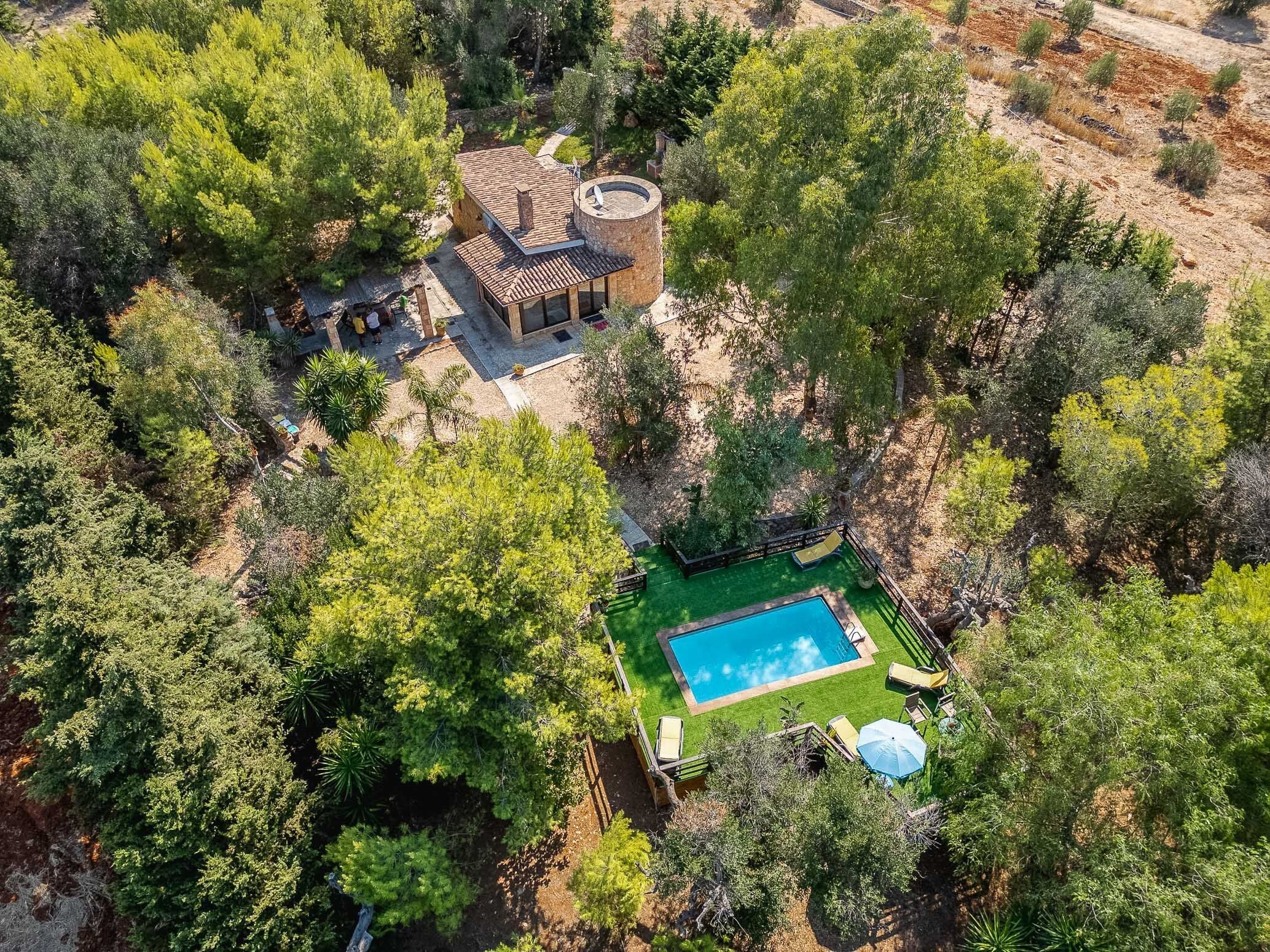 Vista aérea de una propiedad con piscina, zona exterior cubierta y vegetación densa circundante.
