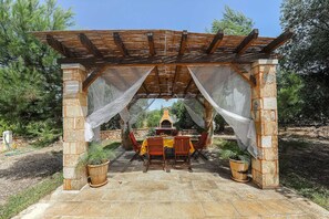 A stone pergola with a table and chairs underneath, surrounded by potted plants. - Torre del Drago - Three Bedroom Villa, Sleeps 6 (Marina di Felloniche)