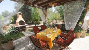 An outdoor patio with a table set for dining, surrounded by chairs, and a wood-fired oven. - Torre del Drago - Three Bedroom Villa, Sleeps 6 (Marina di Felloniche)