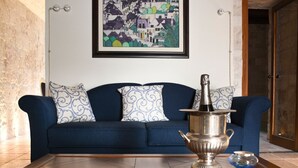 A blue sofa with patterned cushions, a silver decorative pot, and a glass bowl on a wooden table.