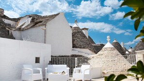 A terrace with white wicker furniture, stone walls, and traditional conical roofs.