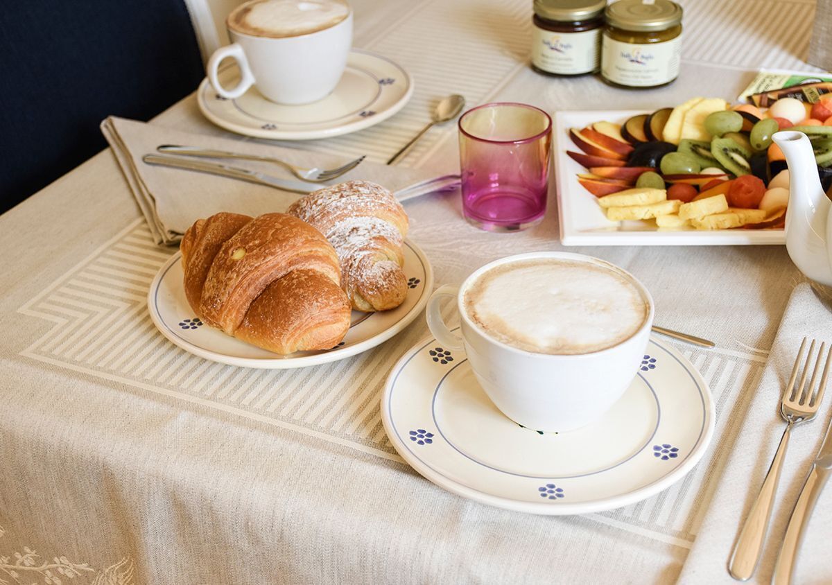 Une table dressée pour le petit-déjeuner, avec des croissants, du café et une assiette de fruits.
