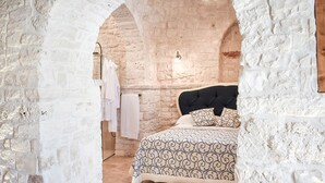 A bedroom with a stone wall, a bed with patterned bedding, and a hanging light fixture.