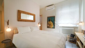 Un dormitorio con una cama grande, lámparas de noche, un espejo con marco de madera, un radiador y un escritorio pequeño con una silla.