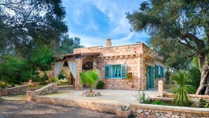 Une maison en pierre avec un toit en tuiles, une entrée couverte et un jardin agrémenté de plantes et d’un palmier.