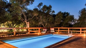 Une piscine rectangulaire entourée d’une terrasse en bois, agrémentée de rampes en bois et de chaises longues.