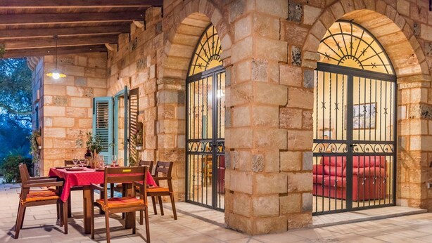 Une terrasse extérieure avec des murs en pierre, une table dressée pour le repas et un canapé rouge.
