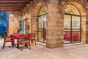 Um pátio externo com paredes de pedra, uma mesa posta para refeições e um sofá vermelho.