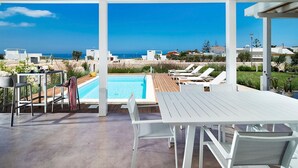 Un espace aménagé au bord de la piscine, avec vue sur la mer, doté de mobilier blanc et d’une structure en forme de pergola.