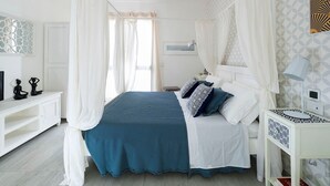 Un dormitorio con cama con dosel, ropa de cama blanca y una mesita de noche con lámpara.