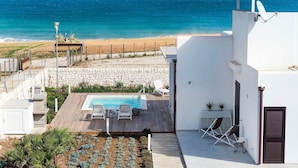 Una piscina al terrat amb gandules, vistes a la platja i un edifici blanc amb antena parabòlica.