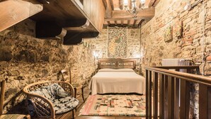 A rustic room with a wooden bed, a wicker chair, and a stone wall. - San Veriano - Five Bedroom Villa, Sleeps 10 (Ripoli)
