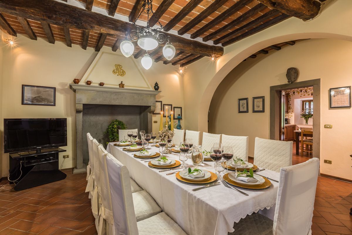 A dining room with a long table set for a meal, a fireplace, and a television.