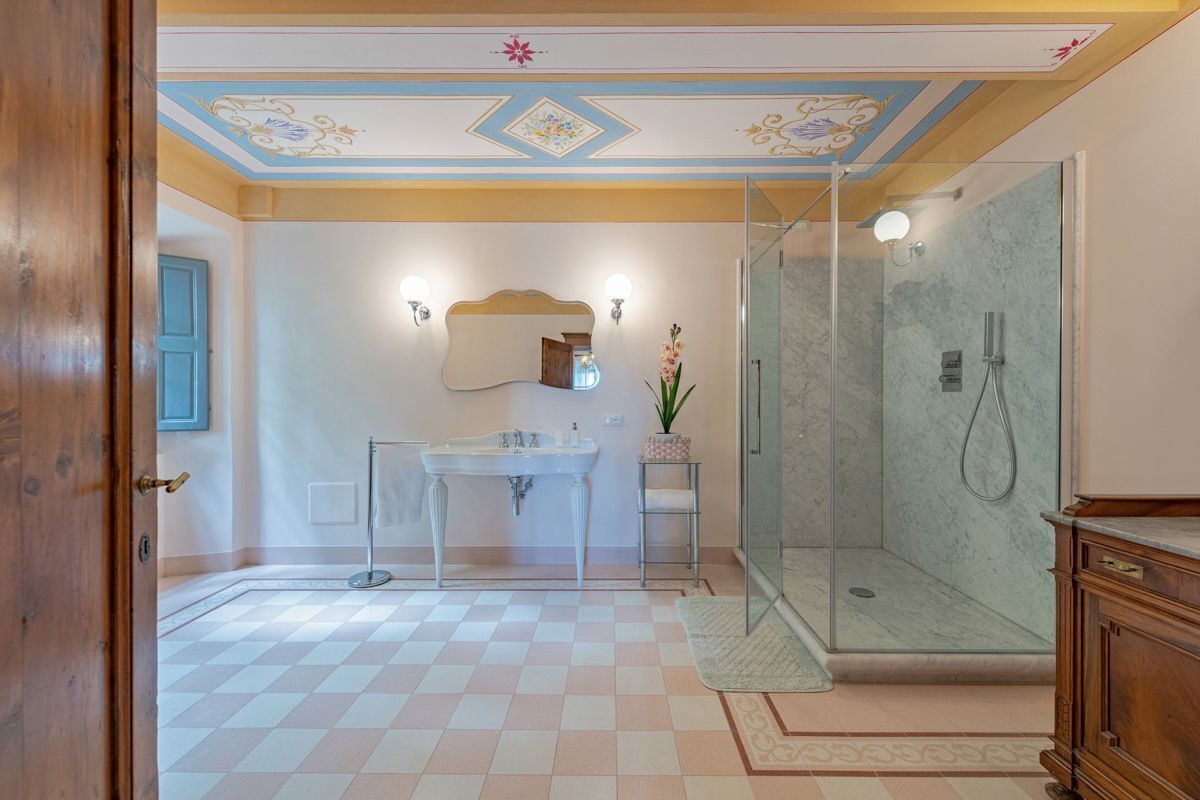 A bathroom with a checkered floor, a glass shower enclosure, a sink with a mirror, and a wooden cabinet.