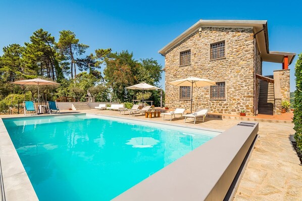 Un bâtiment en pierre doté d’une piscine, d’un espace extérieur aménagé et surplombé d’un ciel bleu azur.