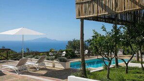 Un espace aménagé au bord de la piscine, avec des chaises longues, une pergola en bois et une vue sur la mer.