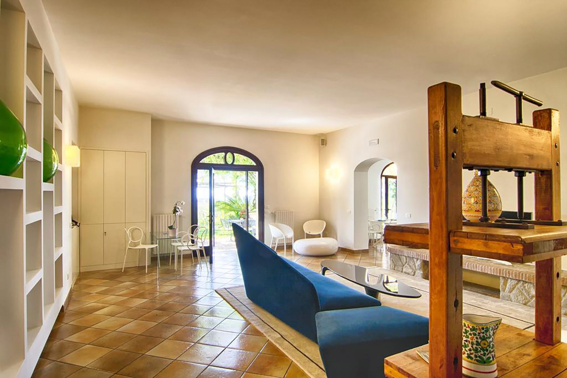 Un'ampia zona giorno con un divano blu, sedie bianche e una scala in legno.